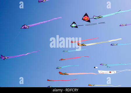 angle view of a colorful kite flying with waving red bow in a deep blue sky with the light of the sun Stock Photo