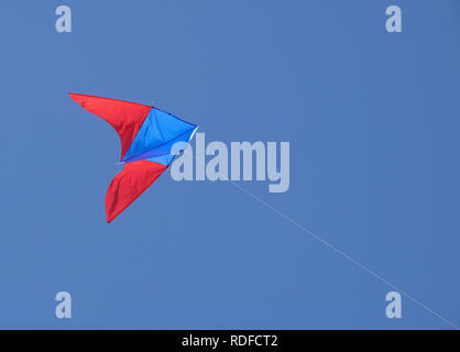 angle view of a colorful kite flying with waving red bow in a deep blue sky with the light of the sun Stock Photo