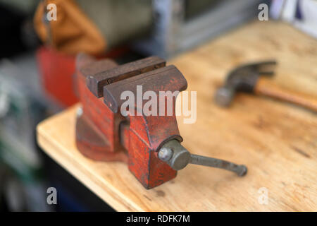 Vintage old red vise on wooden workbench with tools and hammer Stock Photo