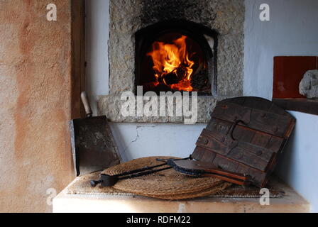 Traditional outdoor firewood oven in countryhouse. Burning flames in fireplace and tools in the foreground Stock Photo