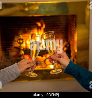 Close up of romantic couple holding two champagne glasses toasting by open wood fireplace celebrating Love happy moments together at cabin in winter h Stock Photo