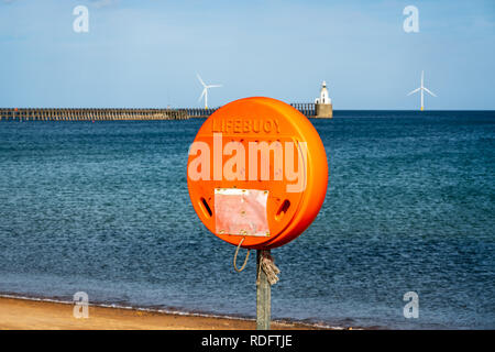 A lifebuoy at North Sea Coast, seen on South Beach in Blyth, England, UK - with Blyth Lighthouse and the pier in the background Stock Photo