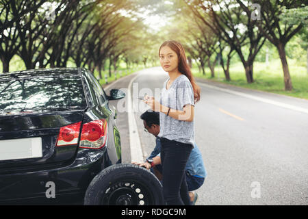 Asian woman using mobile phone while looking and Stressed man sitting after a car breakdown on street Stock Photo