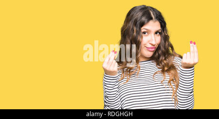 Young beautiful woman wearing stripes sweater Doing money gesture with hand, asking for salary payment, millionaire business Stock Photo