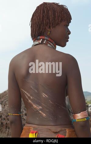 Young Hamar woman with traditional hairstyle with red clay and with scars and marks of being whipped on her back Stock Photo