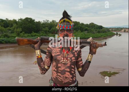 Karo warrior with body and facial paintings and a rifle over the shoulder, Omo river valley, Southern Ethiopia, Africa Stock Photo