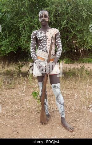 Karo warrior with body and facial paintings holding a rifle, Omo river valley, Southern Ethiopia, Africa Stock Photo