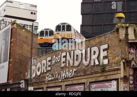 Disused train carriages on top of a building, above a sign that says 'Let's adore and endure each other' in Shoreditch, East London Stock Photo