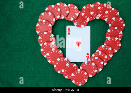 Heart made with poker chips, with an ace of hearts, on a green background table. Top view with copy space. Stock Photo