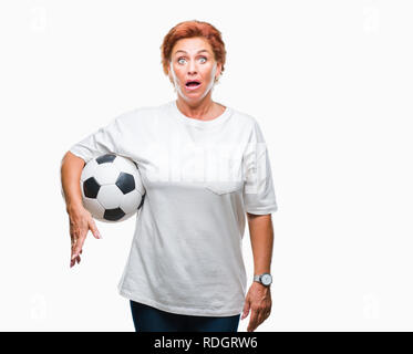 Atrractive senior caucasian redhead woman holding soccer ball over isolated background scared in shock with a surprise face, afraid and excited with f Stock Photo