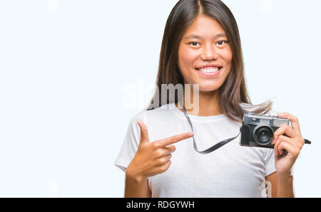 Young asian woman holding vintagera photo camera over isolated background very happy pointing with hand and finger Stock Photo