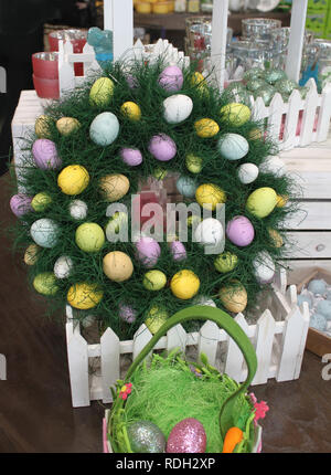 An Easter wreath with colored eggs in a picket fence box surrounded by other Easter decorations and eggs Stock Photo