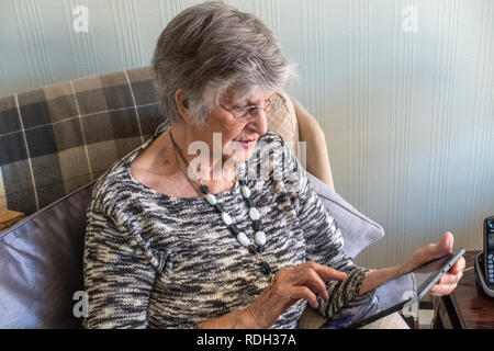 Elderly lady sitting using her personal tablet Stock Photo