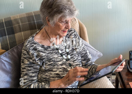Elderly lady sitting using her personal tablet Stock Photo