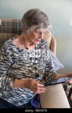 Elderly lady sitting using her personal tablet Stock Photo