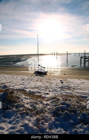 Bay in the Wadden Sea with a sailing boat, snow-covered beach on the East Frisian North Sea island of Spiekeroog, Lower Saxony Stock Photo