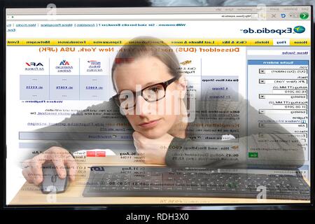 Young woman sitting at a computer surfing the Internet, booking a holiday on a travel portal, Expedia Stock Photo