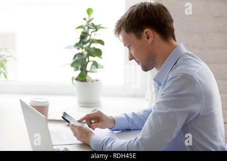 Confident businessman using phone and laptop at workplace Stock Photo