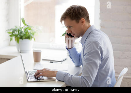 Focused young businessman talking on phone and using laptop Stock Photo