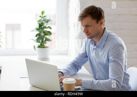 Focused businessman using laptop, looking at screen, doing compu Stock Photo