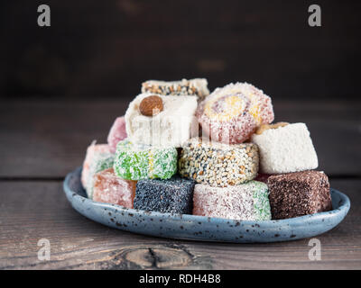Closeup view of assortment turkish delight in blue trandy plate on dark wooden background. Copy space. Low key Stock Photo