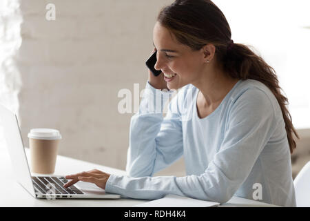 Happy smiling woman talking on phone and using laptop Stock Photo