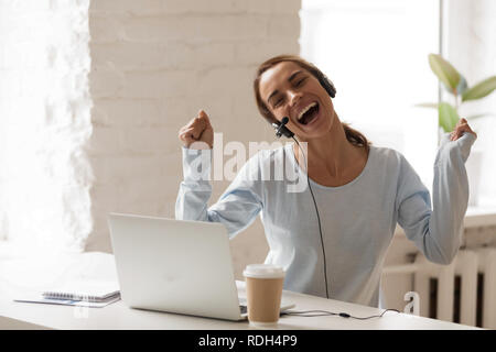 Joyful woman in headphones with microphone using laptop, sing an Stock Photo