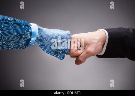 Close-up Of Digital Generated Human Hand And Businessman Making Fist Bump On Grey Background Stock Photo