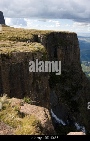 Hikers sit atop Tugela Falls at the Amphitheatre formation in the Drakensberg Mountains, Royal Natal National Park, KwaZulu-Natal, South Africa. Stock Photo