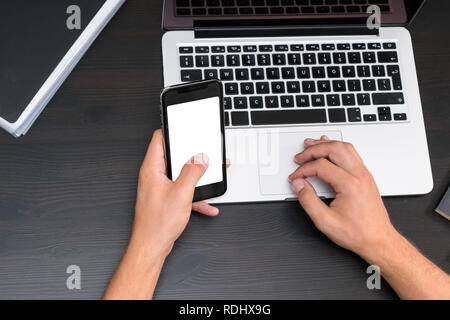 Mans hands typing on smart phone while working on laptop computer on vintage wooden table. Hands typing on a keyboard. Top view, business office workp Stock Photo