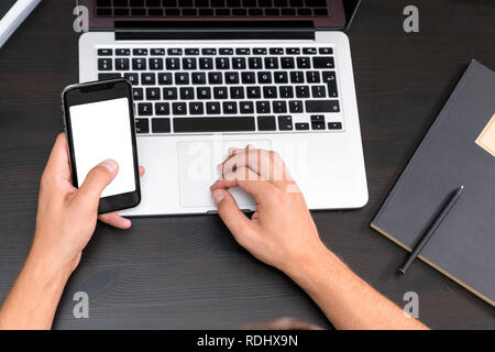 Mans hands typing on smart phone while working on laptop computer on vintage wooden table. Hands typing on a keyboard. Top view, business office workp Stock Photo