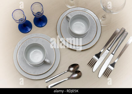 On the table, two cups with saucers, glasses, knives, spoons, forks on a napkin. The view from the top. Stock Photo