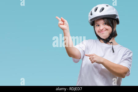 Young adult cyclist woman with down syndrome wearing safety helmet over isolated background smiling and looking at the camera pointing with two hands  Stock Photo