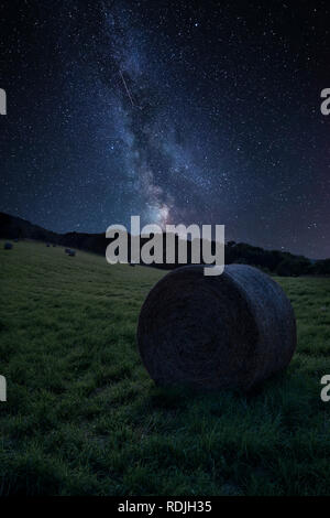 Stunning vibrant Milky Way composite image over landscape of Summer countryside of field with hay bales