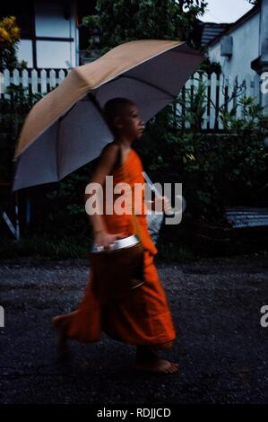 Luang Prabang / Laos - JUL 06 2011: monk during their early morning round around the town to collect their alms with umbrella Stock Photo