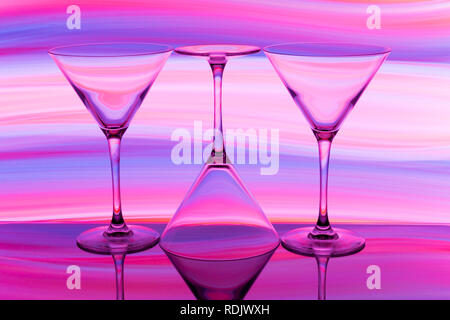 A row of three cocktail / martini glasses in a row with a rainbow of multicolored light painting behind them Stock Photo