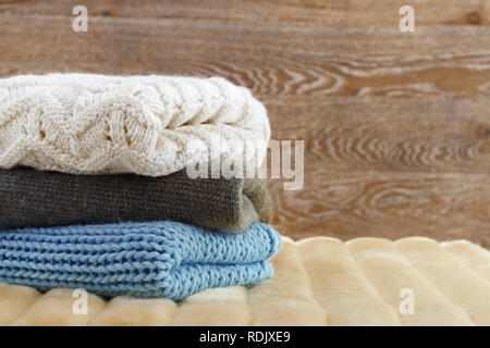 Warm clothing lies in a pile on a fluffy soft rug. Knitted sweaters on a wooden background. Autumn and winter concept Stock Photo