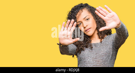 Young beautiful woman with curly hair wearing grey sweater Smiling doing frame using hands palms and fingers, camera perspective Stock Photo