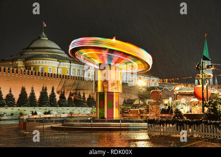 = Colorful Spinning Carousel at the Red Square in Snowfall =  Evening view of the colorful spinning carousel at the corner of the Christmas and New ye Stock Photo