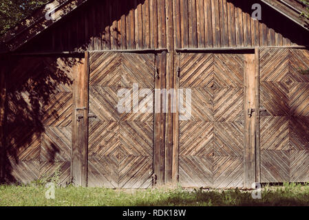 An aged, rural farm building with two doors and rusted locks with a rustic natural wooden facade and decorative woodwork in a creative pattern Stock Photo