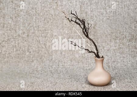 Dry clumsy branches dark and light in a clay jug on the background of the canvas - still life in rustic style Stock Photo