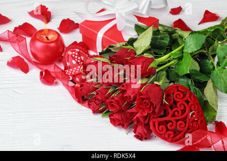 Valentine's Day background with a bouquet of beautiful red roses, gift box, heart shaped ornaments and globe shaped candle on white wooden table (sele Stock Photo