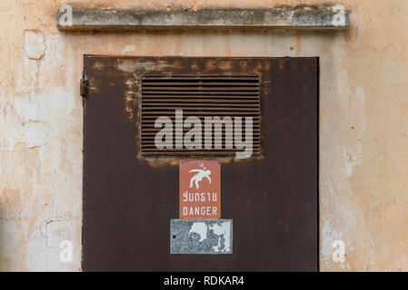 Transformer cabinet with the rusty door & a meaningful sign warns (in Laotian & English) on danger of high voltage. Vientiane, Laos Stock Photo