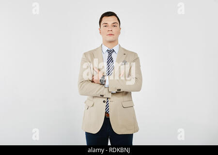 Stylish and handsome young brunet man in the white shirt with striped tie, in a beige blazer and in dark jeans posing at white background, isolated Stock Photo