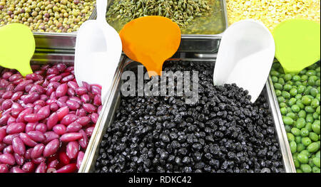 tray filled with black and green olives and other organic products such as red onions for sale in the market stall of a Mediterranean country Stock Photo