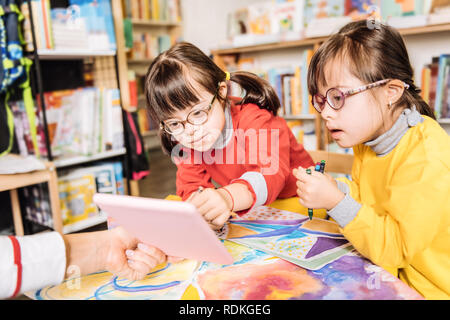Dark-haired preschool girls with Down syndrome having drawing class Stock Photo