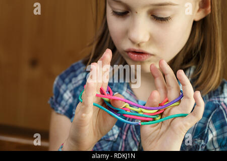 Child playing classic, old-school string game and didactic toy with her fingers, creating shapes, developing her motor skills. IQ, education, intellig Stock Photo