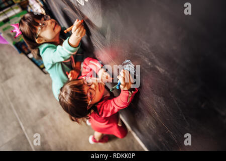 Top view of two sunny children wearing glasses drawing on blackboard Stock Photo