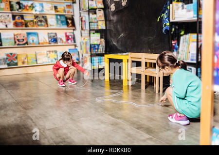 Two sisters wearing the same bright dresses having fun in kids library Stock Photo