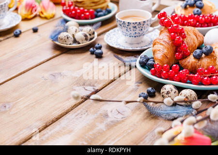 Easter breakfast flat lay with fresh coffee, berries and pastries , orange tulips, croissants with bacon and various sweets , colored quail eggs and s Stock Photo